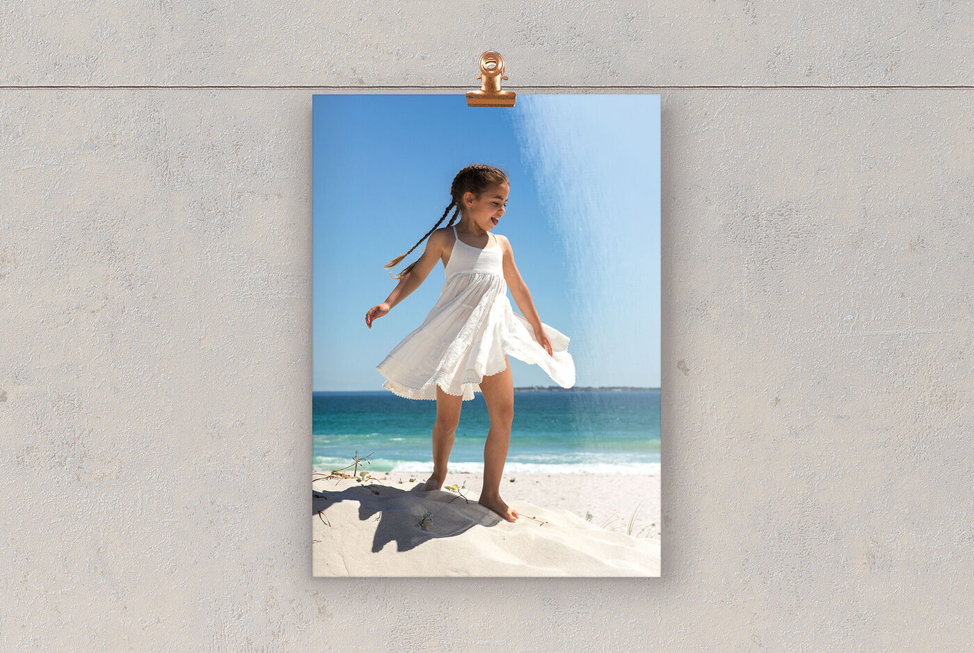 En flicka i vit klänning står lycklig på stranden och njuter av solen.