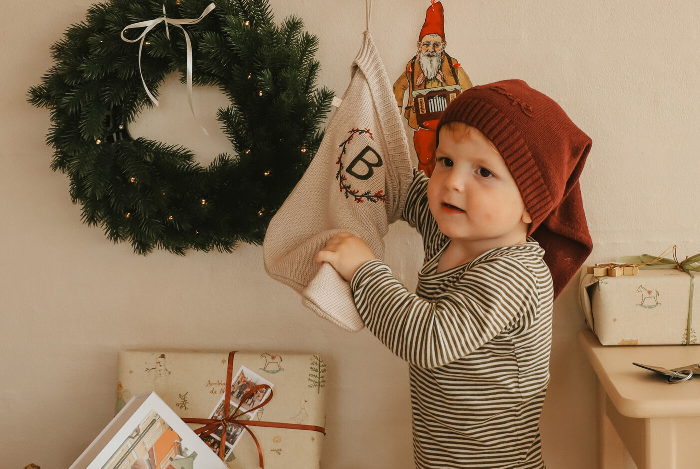 Ett barn hänger en julstrumpa på en vägg med en krans.