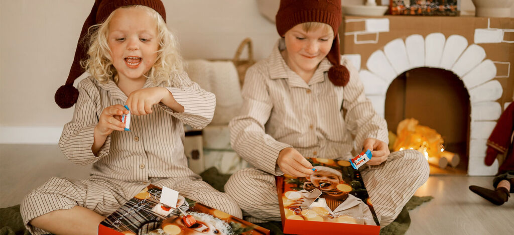 Två barn i pyjamas sitter på golvet och öppnar presenter