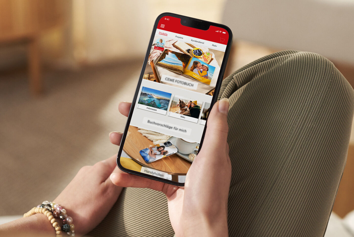 Person håller smartphone med CEWE-appen, visar fotoböcker.